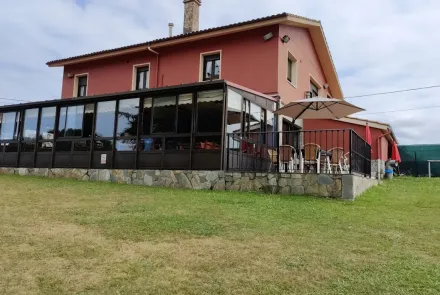 Fachada de bar‑restaurante "La Portiella" con terraza acristalada y jardín